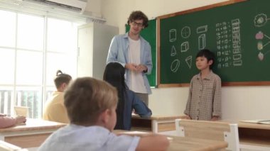 Asyalı bir öğrenci sınıfın önüne geçer ve beyaz bir öğretmen öğrenciye bakıp çocuğu cesaretlendirirken kendini sınıfa tanıtmaya başlar. Çeşitli çocuklar oturur ve oğlanlara bakarlar. Pedagoji.