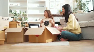 Kutudan kitap seçen ve oturma odasında kitap okuyan mutlu lezbiyen çift. Taşınırken kutular ve mobilyalarla çevrili otururken çekici bir kız konuşuyor ve paketleri açıyor. Yer değiştirin. Myrmidon.