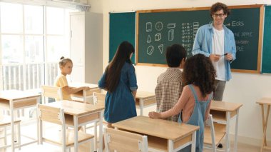 Çeşitli ilkokul öğrencileri öğretmenleri çocuğa bakarken sınıfta yürüyorlar. Profesyonel eğitmen tahtaya çıkıp öğretmenlik yapmaya hazırlanırken sevimli çocuklar sınıfa katılıyor. Pedagoji.