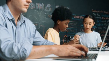 Genç öğrenci BTMM sınıfında öğretmenlik yaparken denetleyiciyi tamir ediyor. Akıllı kız elektronik alet ve karatahta kullanırken eğitmen el bilgisayarı. Öğretim.