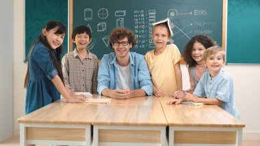 Profesyonel Kafkas öğretmeni ve çeşitli öğrenciler kameraya bakarken mutlu okul çocuğu gülümsüyor. Sınıfın önünde dururken gülümseyen bir grup çok kültürlü çocuk. Eğitim. Pedagoji.