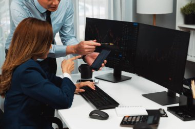 Gülümseyen Asyalı işadamı telefondaki dinamik borsa verilerini bilgisayarda kar değeri değerinin analizi için arayan kadın ortağa gösteriyor. Ofisteki ekranlarla karşılaştırınca. İnfobahn.