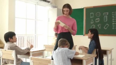 Zeki Asyalı öğrenci, ilkokulda öğretmen yürürken ve ödevlerini kontrol ederken matematik sorusunu sorarak elini kaldırdı. Öğretmen not defterini alırken soruyu cevaplıyor. Pedagoji.