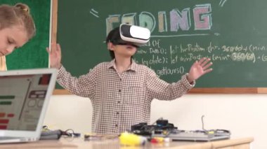 Kız kodlama sistemiyle uğraşırken metaworld 'e elektronik panoyla girmek için VR kulaklık takan bir çocuk. Çeşitli öğrencilerden oluşan bir grup program geliştirmek ve mühendislik kodu yazmak için birlikte çalışıyor. Pedagoji.