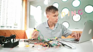 Akıllı mutlu çocuk araba modelini tamir etmek için elektronik alet kullanmayı öğreniyor ya da inceliyor. Lise öğrencisi STEM sınıfında otururken robotik makineleri tamir etmek için elektrikli teçhizat eğitimi alıyor. Öğretim