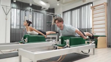 Erkek ve kadın spor salonunda vücut ve sırt kaslarını güçlendirmek için pilates sandalyesi üzerinde egzersiz yapıyorlar. Pilates partneri sırtının üst kısmını güçlendirmek için yenilikçi olmaya eğilimli. Alışkanlık.