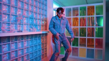 Gece kulübünde kameraya bakarken güneş gözlüklü Asyalı dansçı serbest dans ediyor. Mutlu sokak dansçısı dans ediyor ve renkli parlak neon ışığı ya da yol gösteren ışıkla ayak seslerini gösteriyor. Mutluluk.