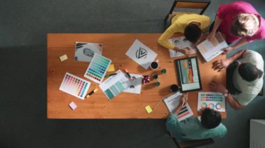 Proje yöneticisi renk paletleri seçerken tasarımcının tablete baktığı yukarıdan aşağıya hava görüntüsü. Profesyonel grafik tasarımının en üst görüntüsü ve logoya bakın. Yetenekli ekip grafikleri seçiyor. Sempozyum.