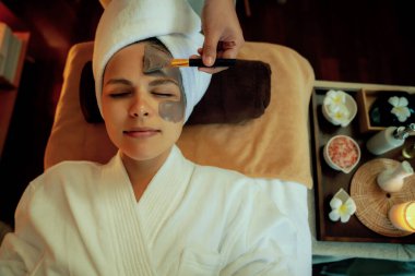 Kaplıca salonunun sakin atmosferi, üst düzey kadın müşteri sıcak mum ışığında kömür kömürü yüz kremi masajıyla kendini yenilemeye çalışıyor. Yüz bakımı ve güzellik konsepti. Sessiz.