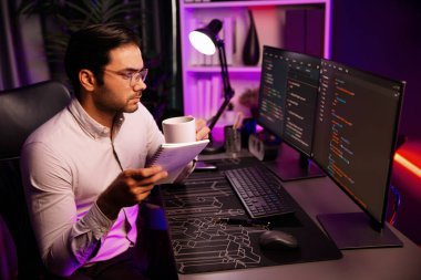 Akıllı bilişim geliştiricisi, bilgisayar ekranındaki yazılım geliştirme kodlaması üzerine kahveyle birlikte çalışıyor, en yeni uygulama projesi programı ile birlikte neon ışıklı siber ofiste çevrimiçi web sitesi verilerini güncelliyor. Tahmin et..