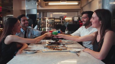 Grup arkadaşının kokteyl içkileriyle tezahürat yapmak. Etrafı ızgara ve kızarmış et menüsüyle çevrili. Birlikte lüks bir restoranda yemek masasında eşsiz bir şef masası menüsü var. Vinosity.