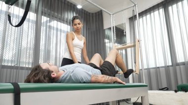 Cadillac ekipmanları üzerinde bacak kaldırma egzersizinde müşteriye yardımcı olan yetenekli pilates eğitmeni. Kadın antrenör, Cadillac 'ın bacak gerdirme hareketine yardım ediyor. Temel bağlantıyı geliştirmek için, bacak esnekliği için. Alışkanlık.