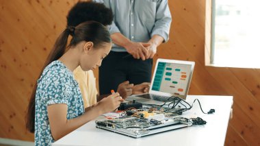 Öğretmen ayakta dururken kodlamayı ve robot yapısını açıkla. Çeşitli gençler ana kartı tamir ediyor ve dizüstü bilgisayarın programlama ekranına bakarken elektronik alet kullanıyorlar. Öğretim.
