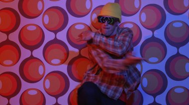 Profesyonel break dansçı, parti sahnesinde balon arka planlı gözlük takıyor. Havalı giyinen yetenekli bir sanatçı enerjik hareketler ve ayak sesleri göstererek müziğe yöneliyor. Mutluluk.