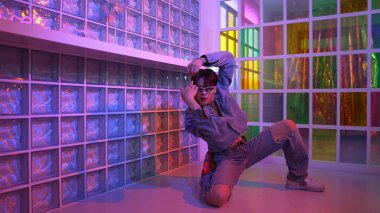 Gece kulübünde kameraya bakarken güneş gözlüklü Asyalı dansçı serbest dans ediyor. Mutlu sokak dansçısı dans ediyor ve renkli parlak neon ışığı ya da yol gösteren ışıkla ayak seslerini gösteriyor. Mutluluk.