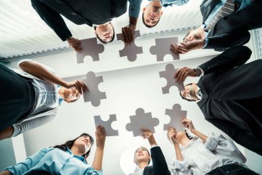 Çok ırklı iş adamları yapboz parçalarını tutuyor ve onları etkili çözüm çözümleri olarak birleştiriyor takım çalışması, ortak görüş ve çeşitli yetenekleri birleştiren ortak hedef. Görüş alanının altında. Habiliment