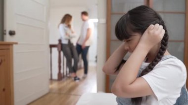 Stresli ve mutsuz genç kız köşeye kıvrılıp kulaklarını kapatarak arka planda ebeveyninin tartışmasını engelliyor. Evde aile içi şiddet ve travmatik çocukluk depresyona dönüşür. Titiz