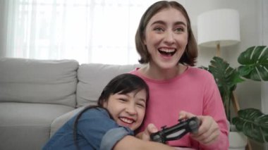 Kafkasyalı bir anne çocuğuna bakıp oyun hakkında konuşurken, mutlu bir kız çocuğu annesinin yanında oturup oyunu kazanıyor. Sevimli kız joystick 'i tut ve başarısını kutla. Pedagoji.