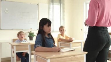 Asyalı mutlu öğrenci ilköğretim sınıfında soruları cevaplamak için gönüllü olurken öğretmen tahtaya cevap yazmak için öğrenciyi seçiyor. Sınıfta çeşitli çocuklar var. Pedagoji.