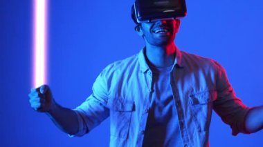 Parlayan kılıcı tutan ve VR gözlük takan oyuncu oyun oynuyor. Çekici erkek model sanal gerçeklik gözlüğü kullanarak yüzen bloğu eskrirken heyecanlanıyor. Teknoloji yeniliği. Aygıt.