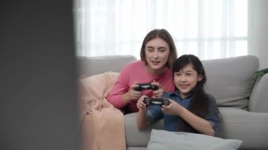 Annem kanepede yatarken, mutlu kız oyun oynuyor ve oturuyor. Beyaz bir ebeveyn ve çekici zeki bir kız elinde joystick ile birlikte vakit geçirip maç kazanmaya odaklanıyor. Yaşam tarzı. Pedagoji.