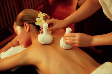 Sıcak bitkisel top spa masaj vücut tedavisi, masör kadın vücuduna nazikçe şifalı bitki torbası bastırıyor. Aromaterapi tesisinin sakinliği ve dinginliği kaplıca salonundaki mumların sıcacık ışığında. Sessiz.