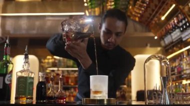 Asyalı barmen soğuk bardağa karışık viski dökerek soğutmalı buzlu içecek üretiyor. Lüks ılık barlarda alkol yenileme gösterisine odaklanan yaratıcı bir reklam yapıyor. Vinosity.