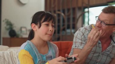 Büyükbaba ve torun birlikte konsol oyunu, eğlence medyası oynuyorlar. Eski kullanım teknolojisi yeni nesil ile iletişim kurar. Nesiller arası uçurum aile bağını güçlendirir. Uyumsuzluk.