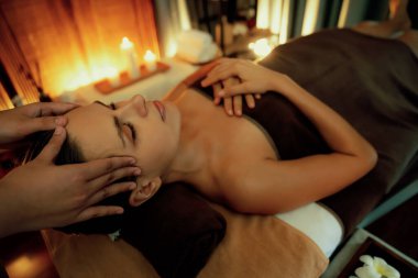 Beyaz kadın stres önleyici kafa masajı yapmaktan ve lüks otel veya otelde sıcak mum ışığında yüz güzelliği eğlencesi yapmaktan zevk alıyor. Sessiz.