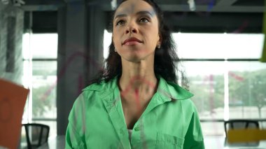 Pazarlama fikrini düşünen yetenekli, genç ve güzel İspanyol proje yöneticisinin portresi. Ofisteki cam tahtada yapışkan notlar kullanarak iş planı yapan profesyonel bir iş kadını. Yönlendirici.