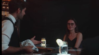 Canlı bir gece partisi atmosferinde lüks bir tezgah barda özel bir içki barında oturan güzel bayan konuğa odaklanıyorum. Müşteriyle konuşurken cam siliyormuş. Vinosity.