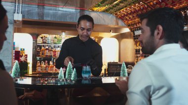 Lüks bar tezgahında kırmızı kurutulmuş meyve biberiyesiyle Noel mavisi lagün kokteylini süsleyen barmen ve VIP grup arkadaşı veya çift yeşil neon Noel ağacı festivaline ev sahipliği yapıyor. Vinosity.