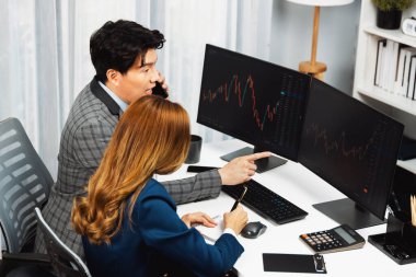 Gülümseyen Asyalı işadamı komisyoncu dinamik borsa veritabanını arıyor. Kadın iş ortağı, iç işyerindeki kar eden uygulama programını karşılaştıran ekranlara işaret ediyor. İnfobahn.