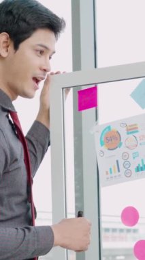 İş adamları ofisteki proje planlama kurulunda çalışıyor ve proje gelişimini analiz etmek için iş arkadaşlarıyla sohbet ediyorlar. Düzenli olması için cam duvara yapıştırılmış yapışkan notlar kullanıyorlar. .