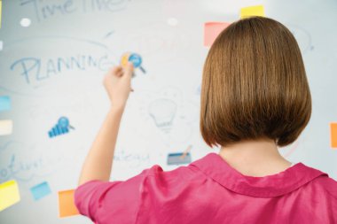 Güzel iş kadını, zihin haritası ve yapışkan notla yaratıcı pazarlama stratejisini düşünürken cam panoya etiket yapıştırıyor. Yaratıcı iş toplantısı konsepti. Arkadan bak. Tertemiz..