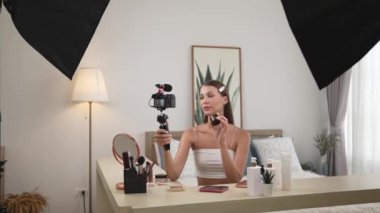 Sosyal medya için güzellik ve kozmetik video içeriği hazırlayan genç bir kadın. Güzellik blogcusu kameraya gülümserken seyircilere ve takipçilere güzellik bakımını gösteriyor. Düzenle