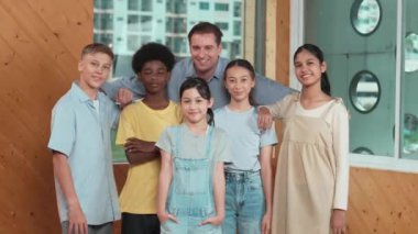 Mutlu öğretmen ve çeşitli öğrenciler kameraya gülümserken ayakta duruyorlar. Profesyonel akıllı eğitmen ve karışık ırk olan lise öğrencileri kameraya neşeli pozlar veriyor. Öğretim