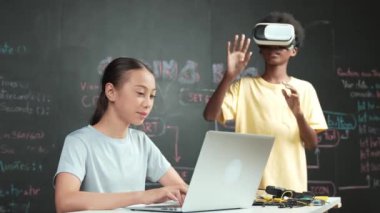 Genç ve güzel akademik öğrenci yazma, kodlama ve programlama sistemini bilgisayarı ya da aygıtı olan masaya yerleştirirken Afrikalı çocuk metaevrene girmek için kulaklık takıyor. yenilikçi eğitim. Öğretim