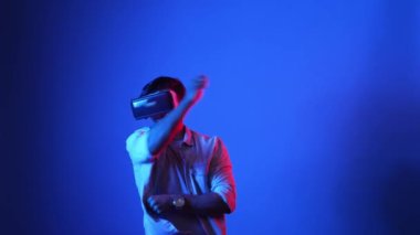 Sanal dünyada kılıç ve eskrim yaparken VR gözlük takan zeki bir oyuncu. Çekici erkek model, mavi arka planda dikilirken ve metaevrene erişirken aksiyon oyunu oynuyor. Aygıt.