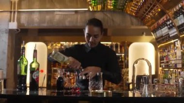 Güzel görünümlü Asyalı barmen içki şurubunu kullanarak lüks içki tezgahında cam hazırlama, gece kulübü lüksündeki düzgün profesyonel barmen kostümü yapıyor. Vinosity.