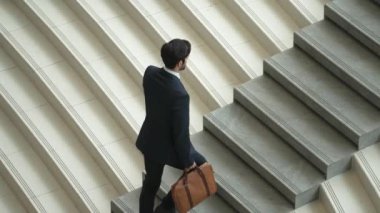 Akıllı bir iş adamının elinde çantayla merdivenlerden yukarı çıkışının en üst görüntüsü. Profesyonel proje yöneticisi merdivenlerden çıkıp işyerine gidiyor. Yeteneklerini arttırmak, terfi almak, seyahat etmek. Sevinçli..