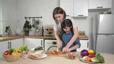 Zeki beyaz anne ve Asyalı kız birlikte yemek pişiriyor ve sebze doğruyor ya da akşam yemeği için salata hazırlıyor. Mutlu anne ve kız taze yemekle sağlıklı yemek yapıyorlar. Sağlıklı gıda konsepti. Pedagoji.