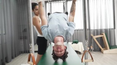 Eğitmen rehberliğinde Pilates Cadillac 'ta ters bacak yükseltme pratiği yapan sağlıklı bir müşteri. Çekirdek dayanıklılığını ve üst vücut dengesini arttırmak için Cadillac 'ı geren adam. Alışkanlık.