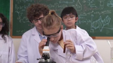 Kafkasyalı öğrenci kimyasal çözüm hazırlarken, yetenekli çocuklar mikroskop altında bakıyorlar. Profesyonel öğretmen, tahtada otururken deney yapıyor. Pedagoji.