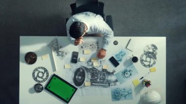 Türbin motoru veya jet motoru tasarımı ve çeşitli metal teçhizat dağılımı ile toplantı masasında yeşil ekranlı tablet üzerinde çalışırken telefona bakan mühendis görüntüsü. Hizalama.