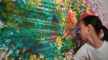 Genç mutlu kız renk tepsisini tutuyor ve fikri ifade etmek ve el iziyle hayal gücünü geliştirmek için renkli duvarları boyuyor. Resim dersinde odayı dekore etmek için beyaz kız pulu. Öğretim