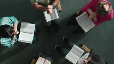 Katlanmış eller yaparken, kucağında haçla İncil okuyan duaların en üstteki görüntüsü. İnanç, güven ve umutla Tanrı 'ya dua eden farklı insanların havadan görünüşü. Ve daireler çizerek oturuyor. Sempozyum.