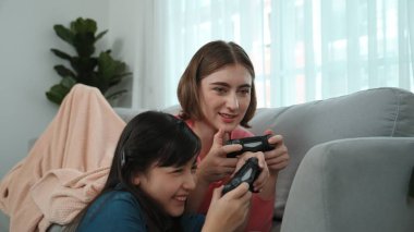 Annem dizüstü bilgisayar kullanarak kanepeye uzanırken, mutlu kız oyun oynuyor ve oturuyor. Beyaz bir ebeveyn ve çekici bir kız, elinde joystick ile birlikte vakit geçirir ve maç kazanmaya odaklanırlar. Pedagoji.