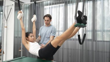 Pilates eğitmeni, Cadillac teçhizatı üzerinde asılı duran bir bacak egzersizinde bir müşteriye rehberlik ediyor. Vücut dengesini sağlamak için Cadillac 'ı geren sağlıklı bir kadın. Alışkanlık.