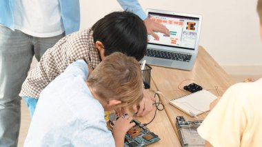 Group of diverse student working together on main board with laptop screen display engineering prompt written while teacher hold tablet and explain online software at STEM technology class. Pedagogy. clipart